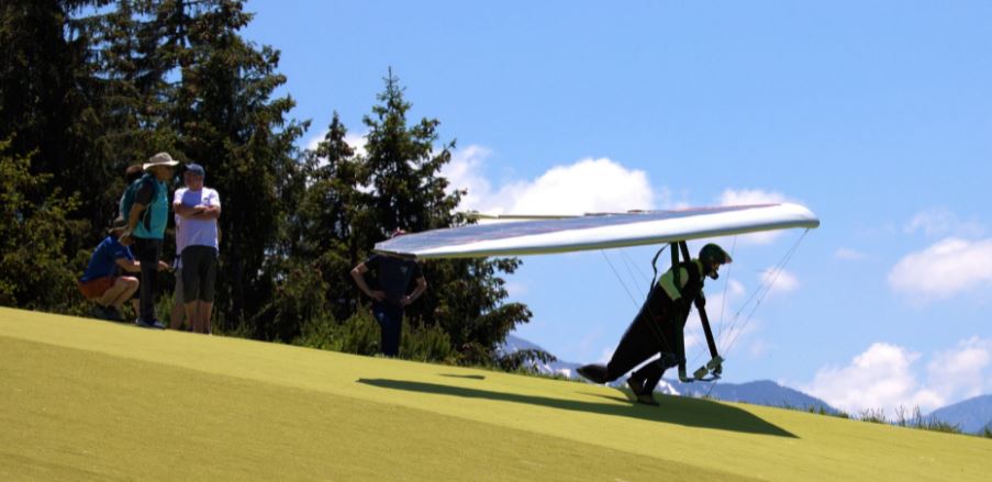 a person wearing hang gliding gear on a mountain about to hang glide, other people at the back
