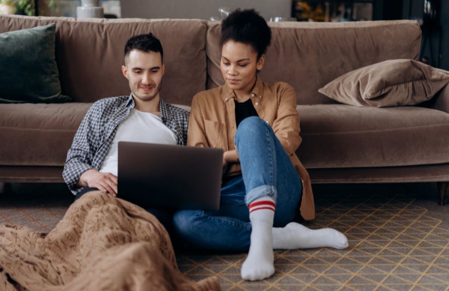 A man and a woman sitting on the floor while looking at the screen of a laptop