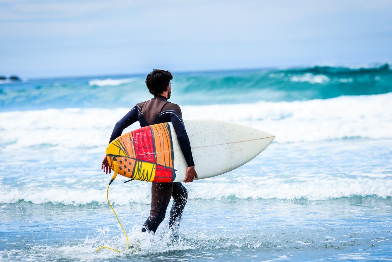 Surfer guy with surfboard in hand running towards big waves