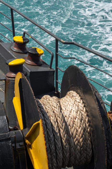 A heavy-duty marine winch with a thick rope is mounted on a ship deck, with the open sea in the background, symbolizing maritime work, transport, and nautical operations