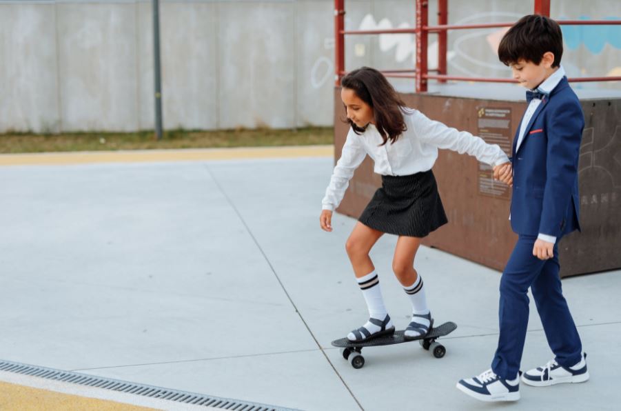 a girl holding the hand of a boy while riding a skateboard