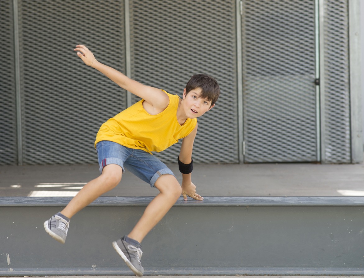 Front view of smiling boy jumping over a metallic fence while looking camera on a bright day