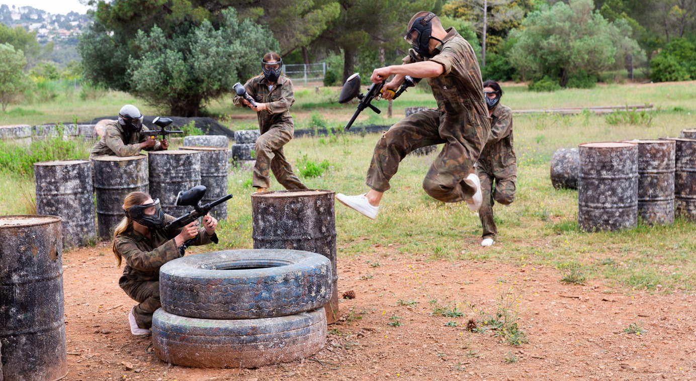 Excited male and female paintball players in protective uniform aiming and shooting with guns