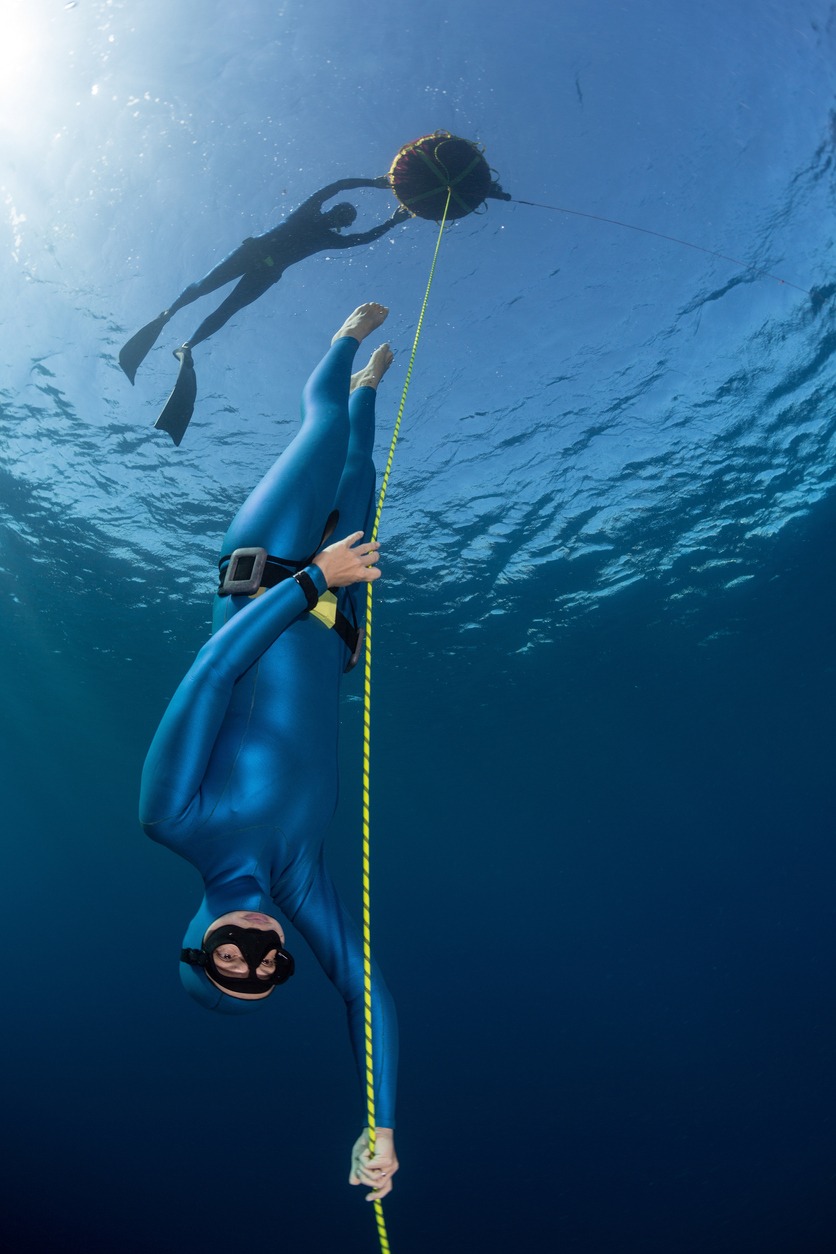 Lady free diver descending along the rope linked to the buoy on surface.