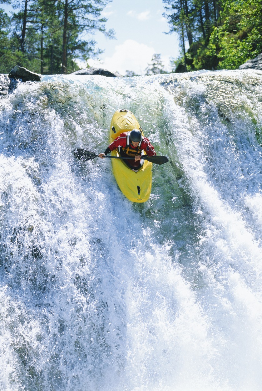 Young man kayaking down waterfall