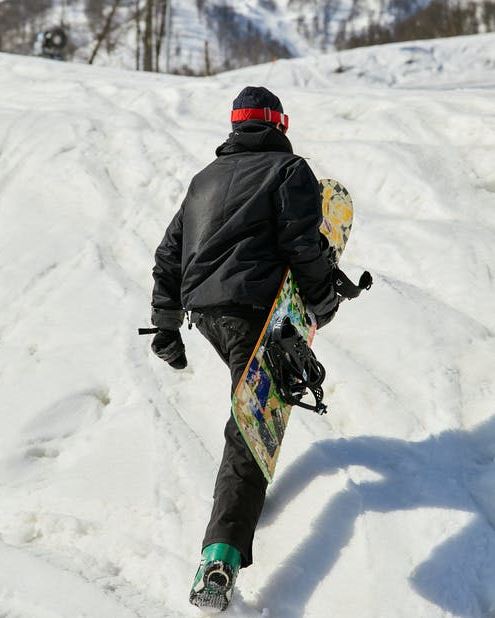 A man walking on the snowy ground while carrying his snowboard